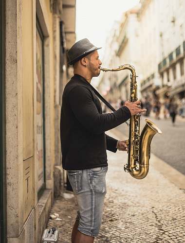 musical instrument man playing copper-colored saxophone on street during daytime saxophone
